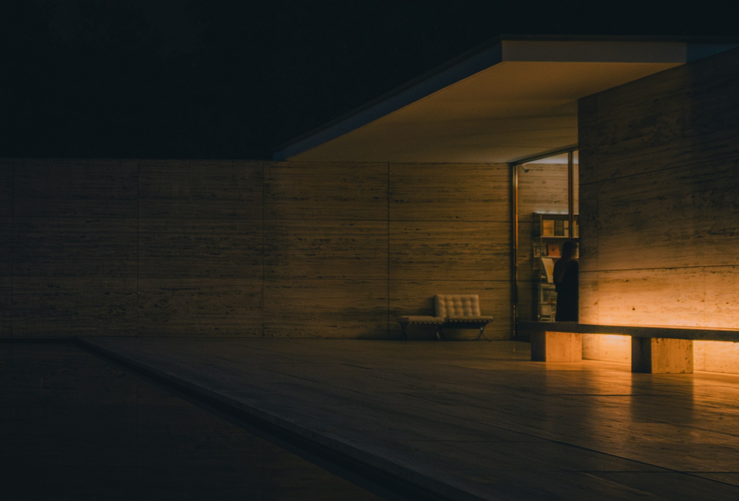 Pátio de arquitetura moderna à noite, com uma sala acesa ao fundo